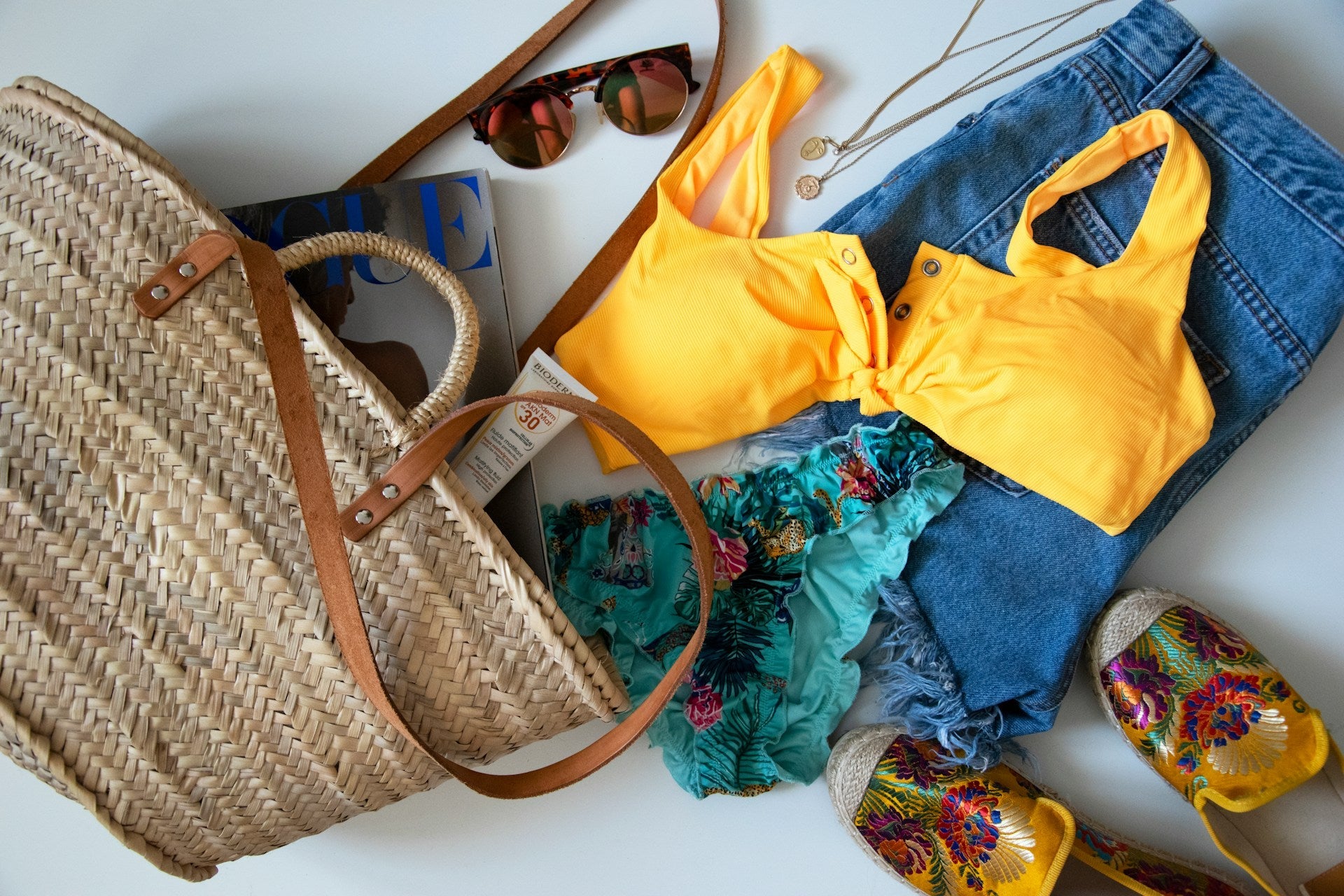 Beach bag styled with sunglasses, sunscreen, and colourful bikinis, showcasing the best beachwear for a summer getaway.