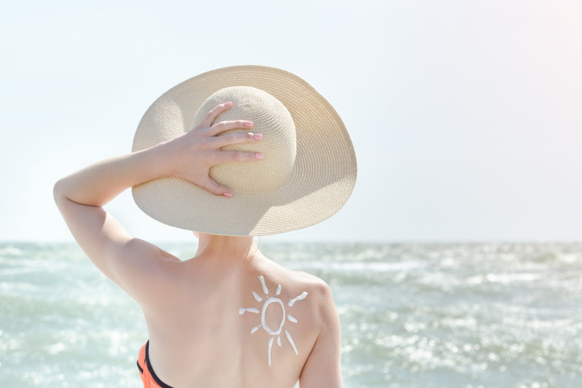 Woman at the beach wearing a wide-brim hat, showcasing swimwear colours for fair skin tones in a coastal setting.
