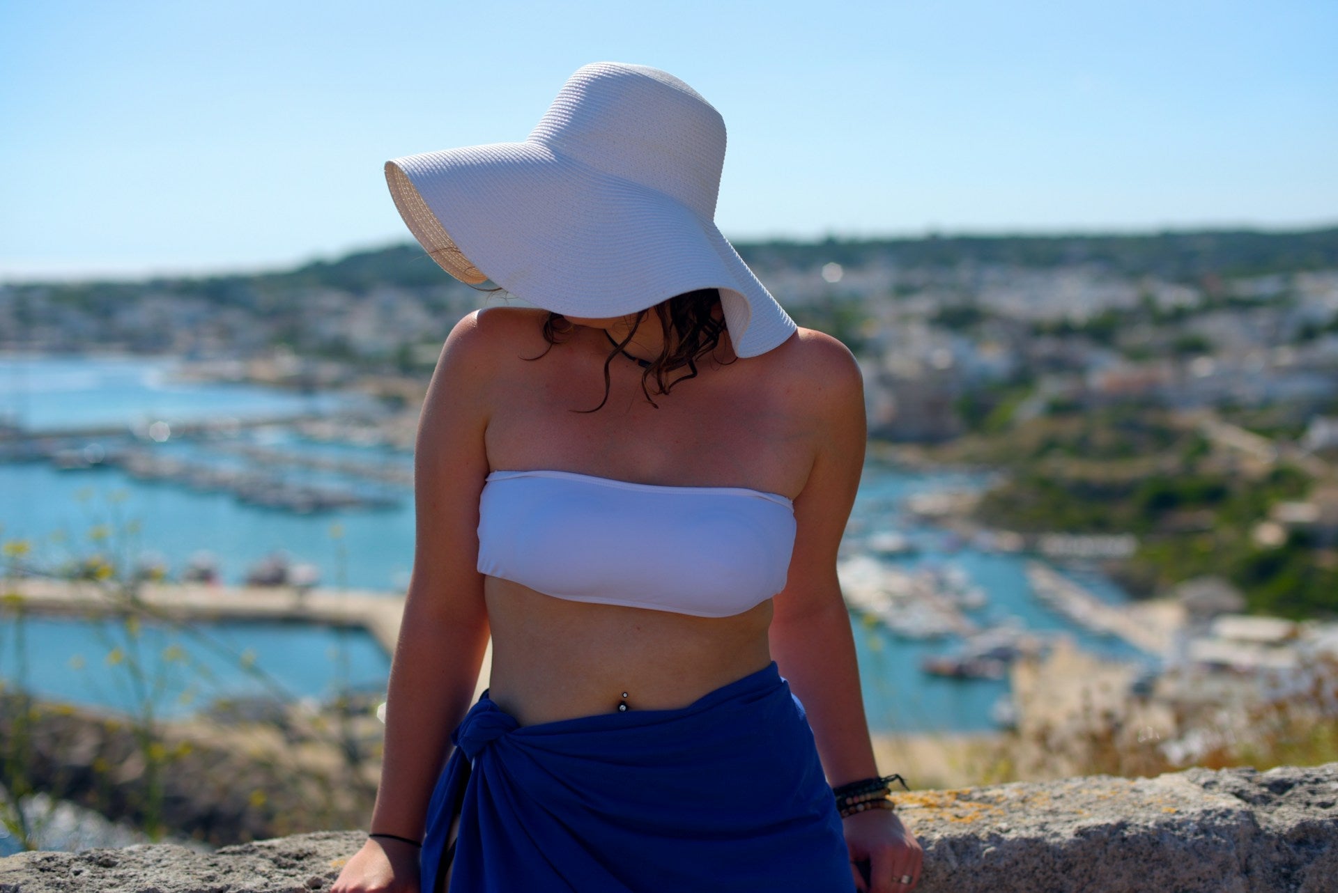 Woman in a wide-brimmed hat, showcasing tube bikinis on a coastal clifftop.